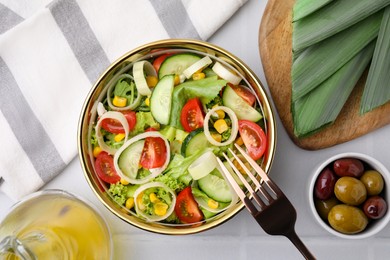 Bowl of tasty salad with leek, tomatoes and cucumbers on white tiled table, flat lay