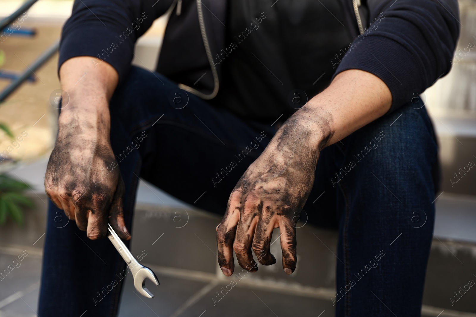 Photo of Dirty worker holding wrench on stairs, closeup of hands