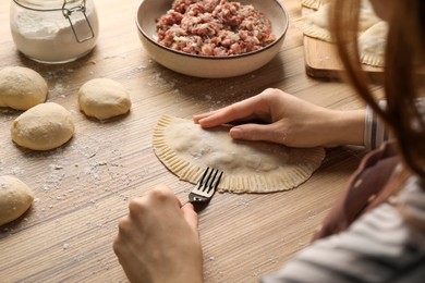 Woman making chebureki with tasty filling at wooden table, closeup