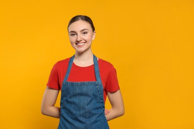 Photo of Beautiful young woman in clean denim apron on orange background