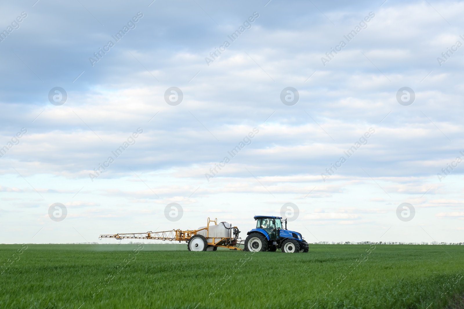 Photo of Tractor spraying pesticide in field on spring day. Agricultural industry