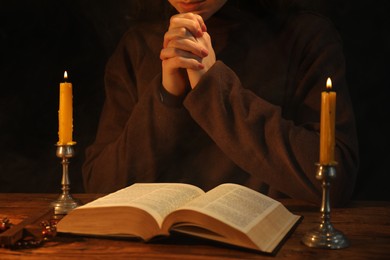 Photo of Woman praying at table with burning candles and Bible, closeup