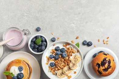 Different tasty dishes with blueberries on grey table, flat lay. Space for text