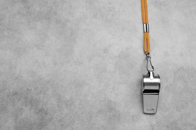 Photo of One metal whistle with cord on light grey table, top view. Space for text