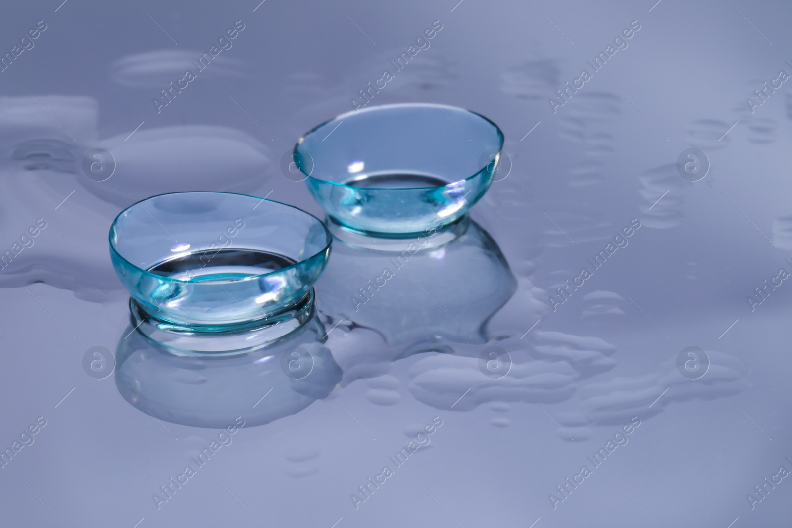 Photo of Contact lenses and drops of water on light reflective surface. Space for text