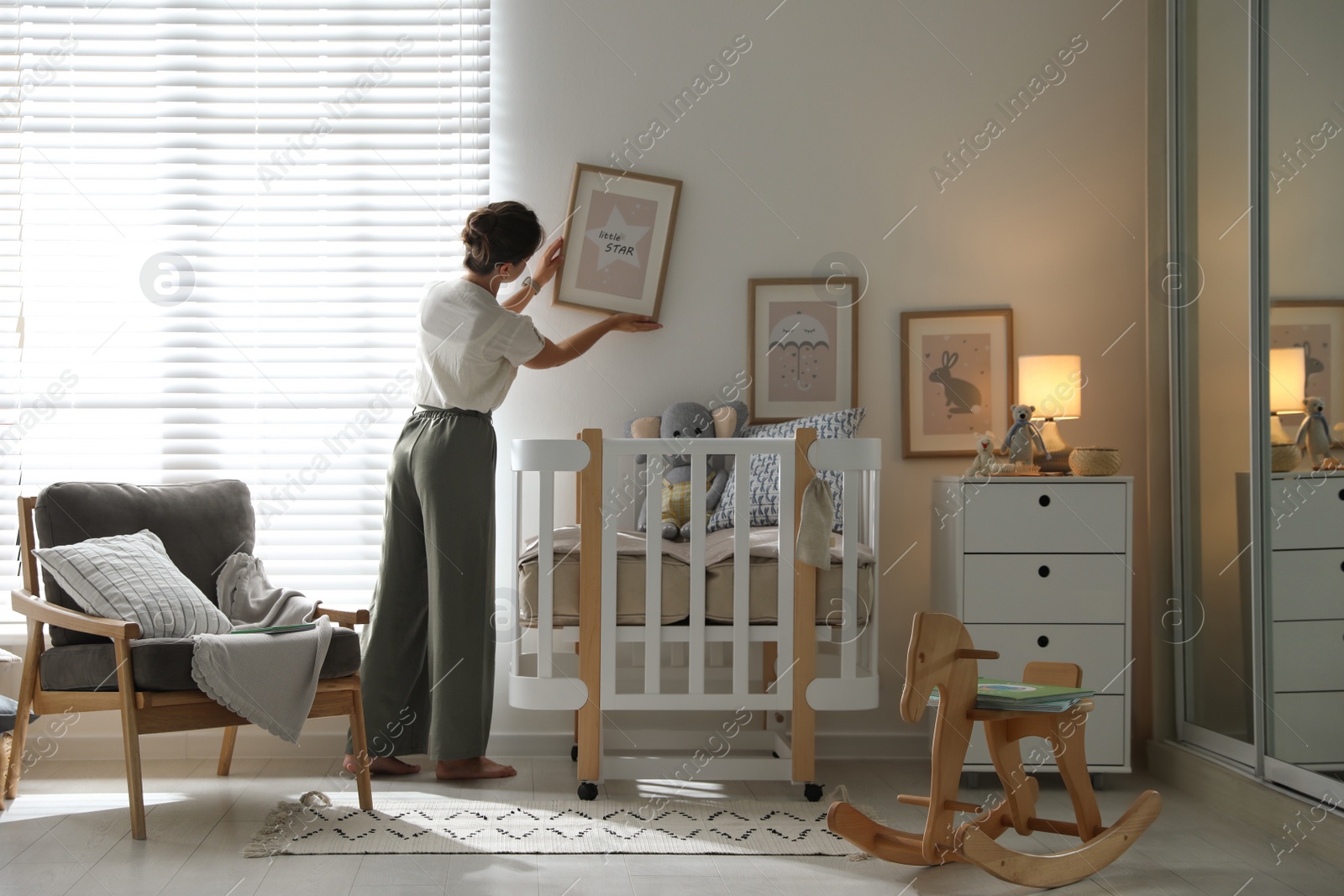 Photo of Decorator hanging picture on wall in baby room. Interior design