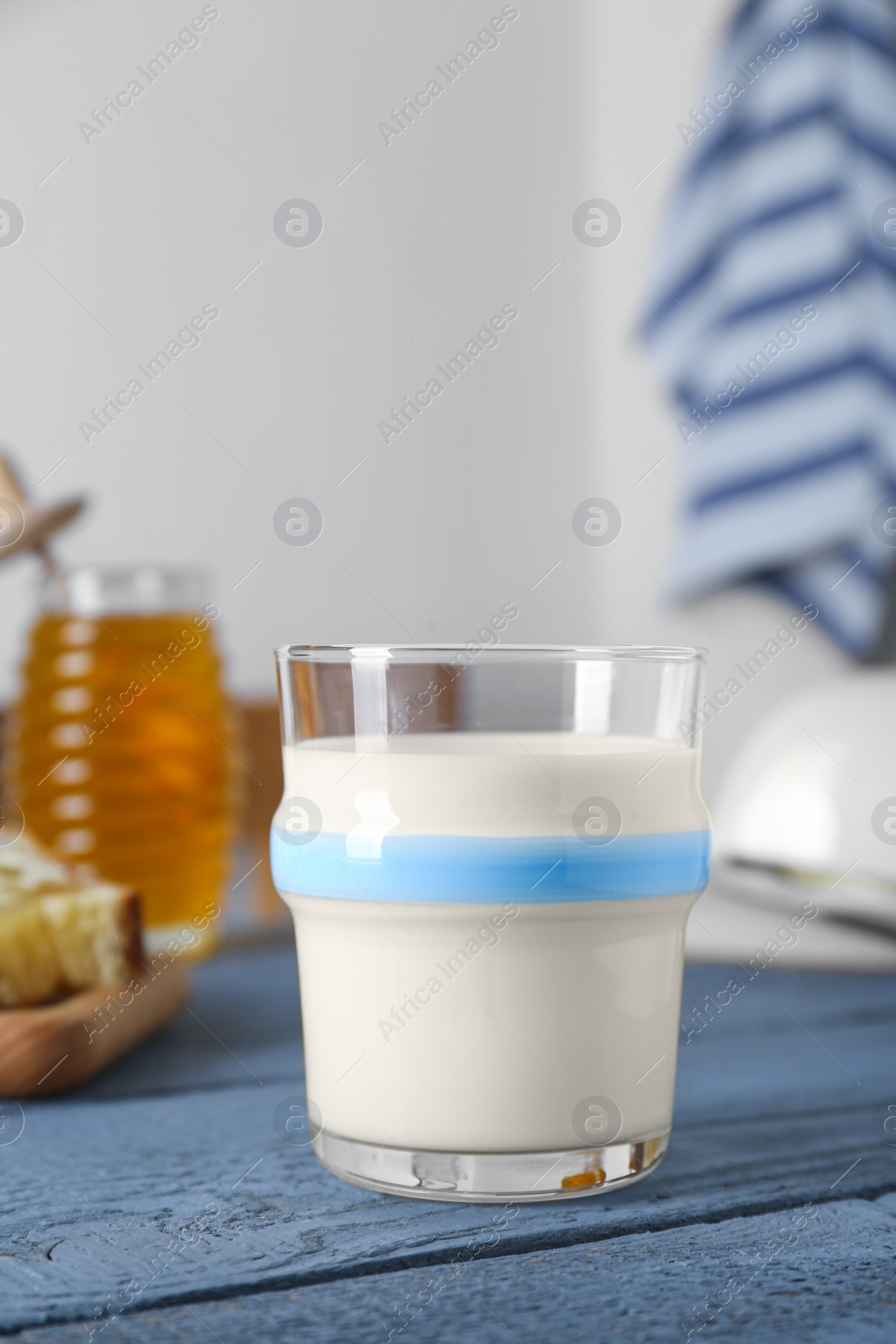 Photo of Glass with milk, honey, bread and butter on grey wooden table