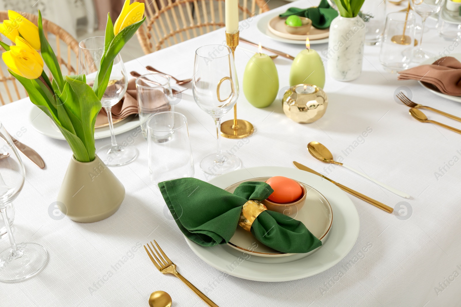 Photo of Festive Easter table setting with painted eggs, burning candles and yellow tulips