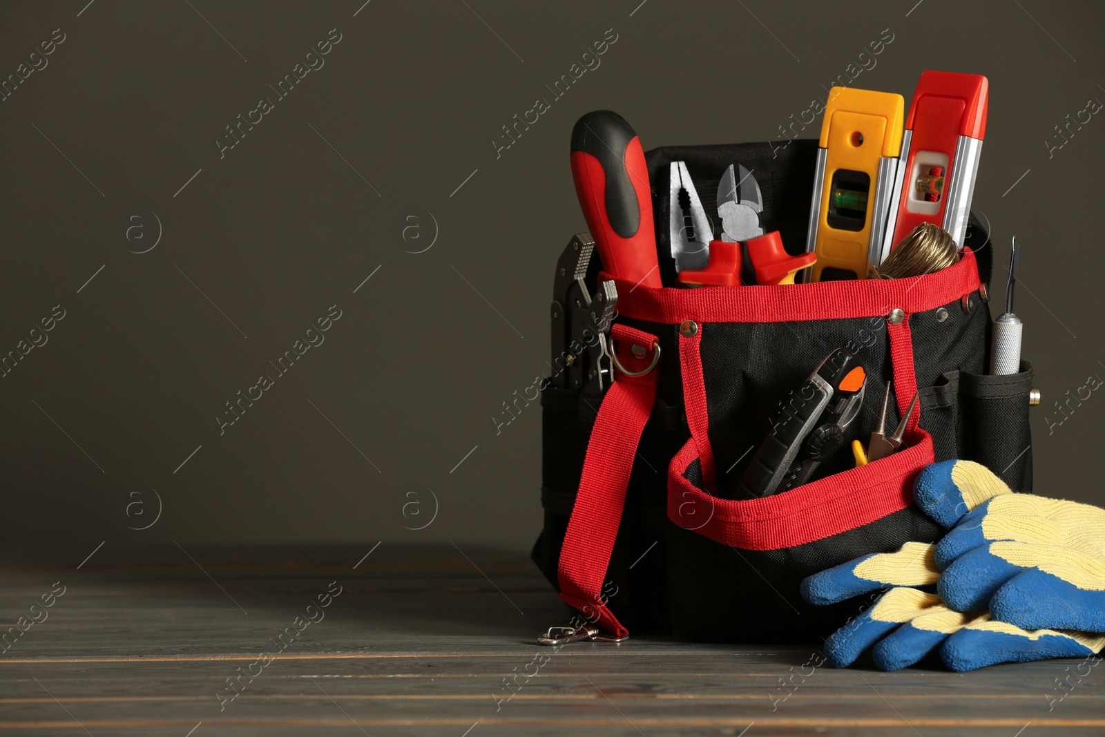 Photo of Bag with different tools for repair and protective gloves on wooden table, space for text