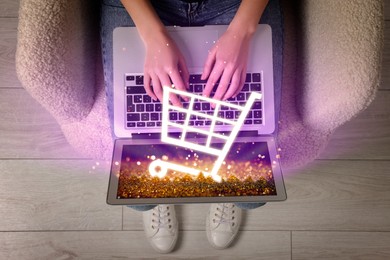 Image of Woman using laptop for online purchases indoors, top view. Illustration of shopping cart icon popping out of device screen