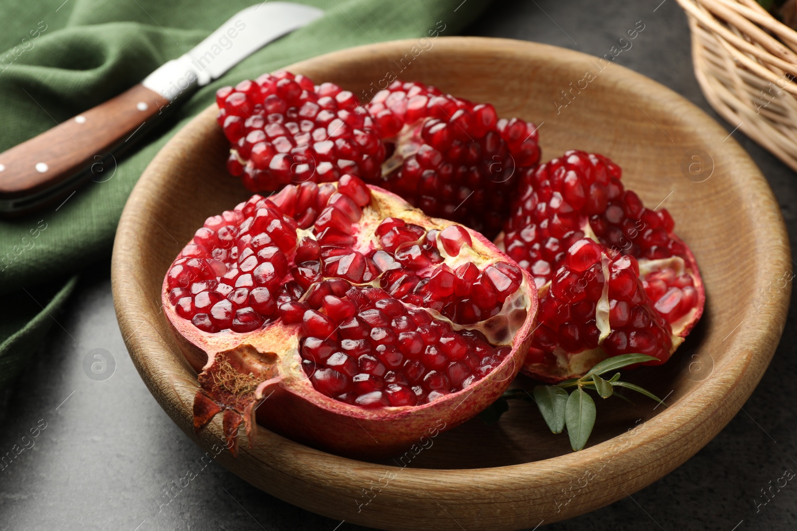 Photo of Cut fresh pomegranate, green leaves and knife on grey table, closeup