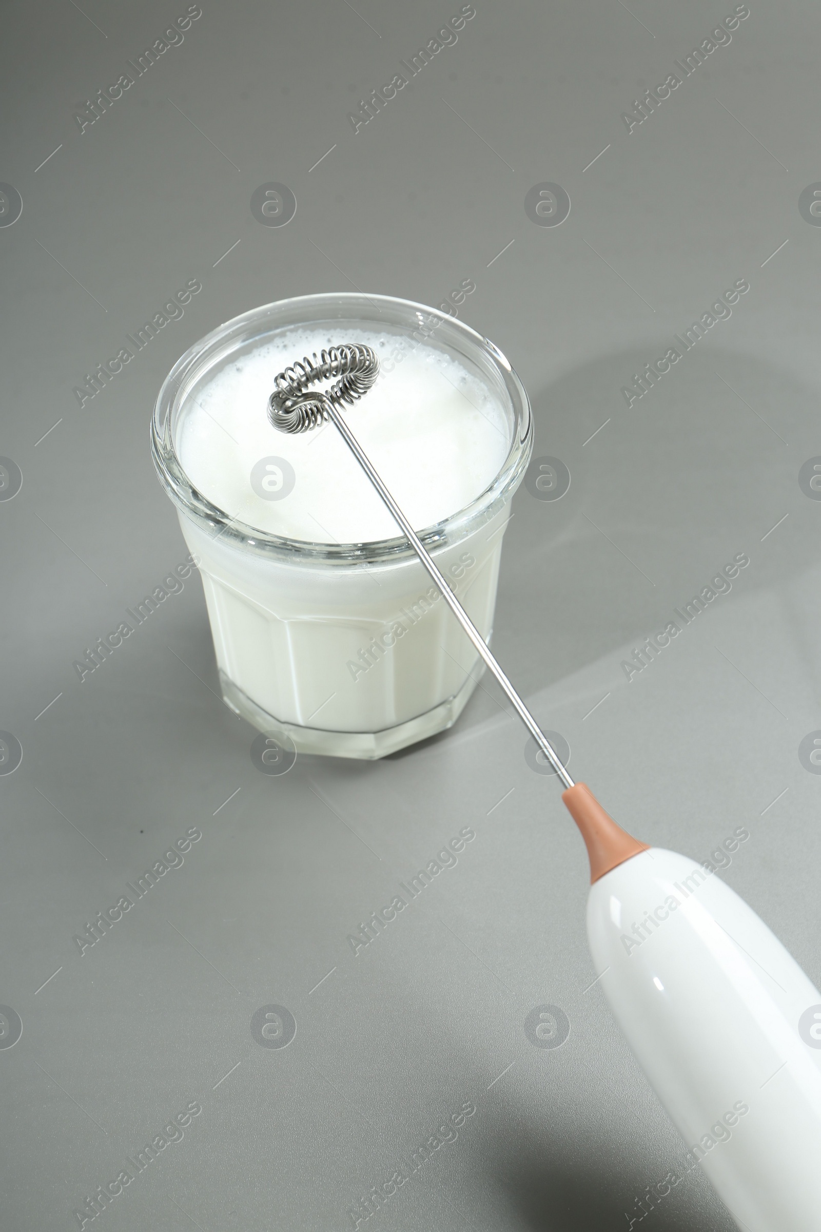 Photo of Mini mixer (milk frother) and whipped milk in glass on grey background