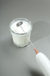 Photo of Mini mixer (milk frother) and whipped milk in glass on grey background