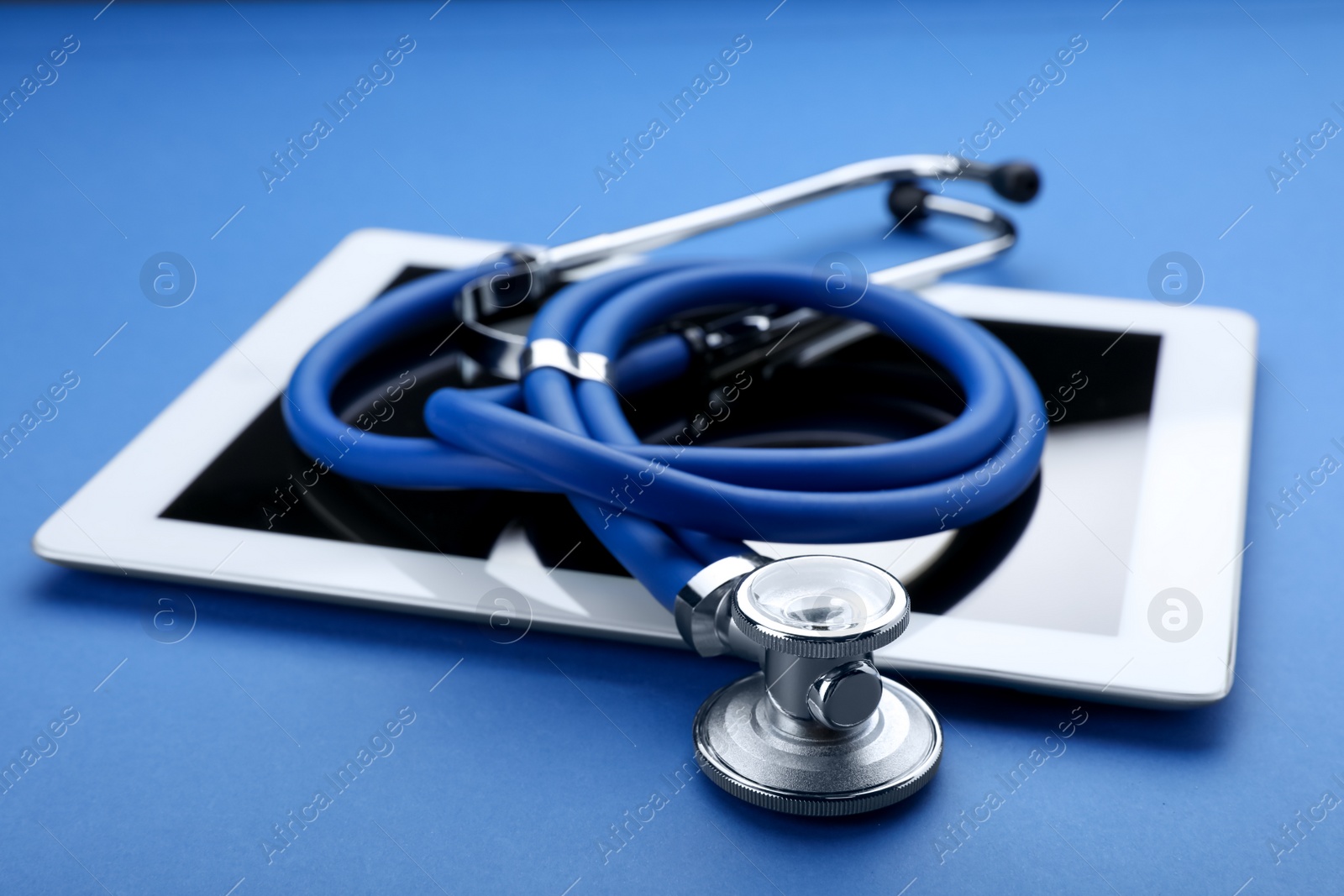 Photo of Computer tablet with stethoscope on blue background, closeup