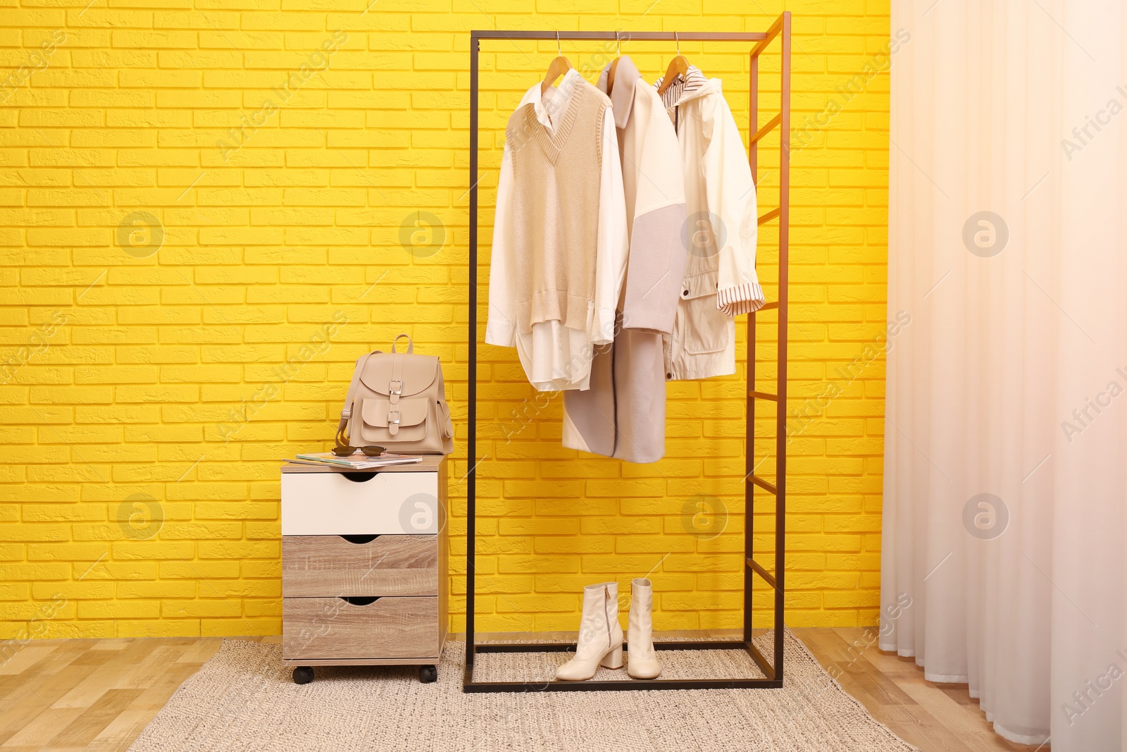 Photo of Rack with stylish clothes near yellow brick wall indoors