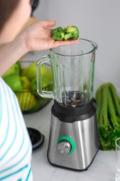 Photo of Woman adding broccoli into blender for smoothie in kitchen, closeup