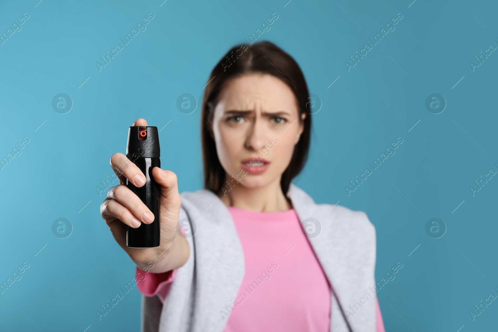 Photo of Young woman using pepper spray on light blue background