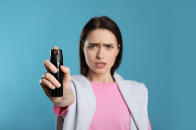 Photo of Young woman using pepper spray on light blue background