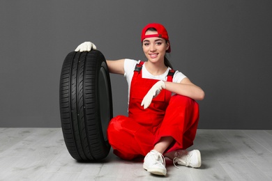 Photo of Female mechanic in uniform with car tire on grey wall background