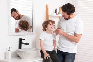 Photo of Father helping his son to brush teeth in bathroom