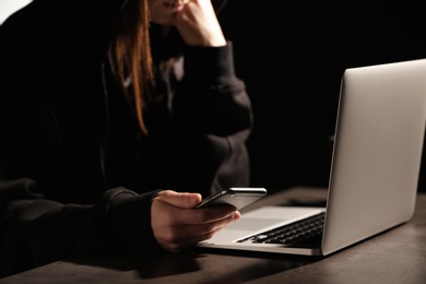 Photo of Woman using smartphone at table with laptop in darkness, closeup. Loneliness concept