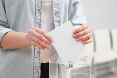 Photo of Woman putting her vote into ballot box on blurred background, closeup