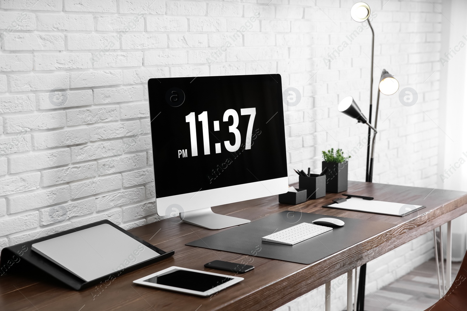 Photo of Modern workplace interior with computer and devices on table near brick wall