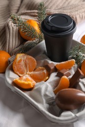 Photo of Delicious ripe tangerines, cup with drink and chocolates on white bedsheet
