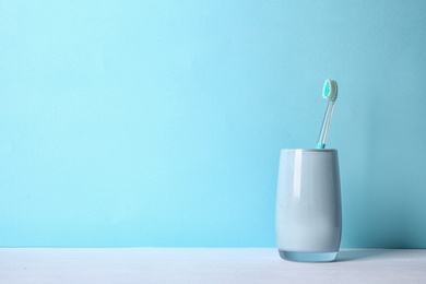 Photo of Cup with toothbrush on table against color background. Dental care