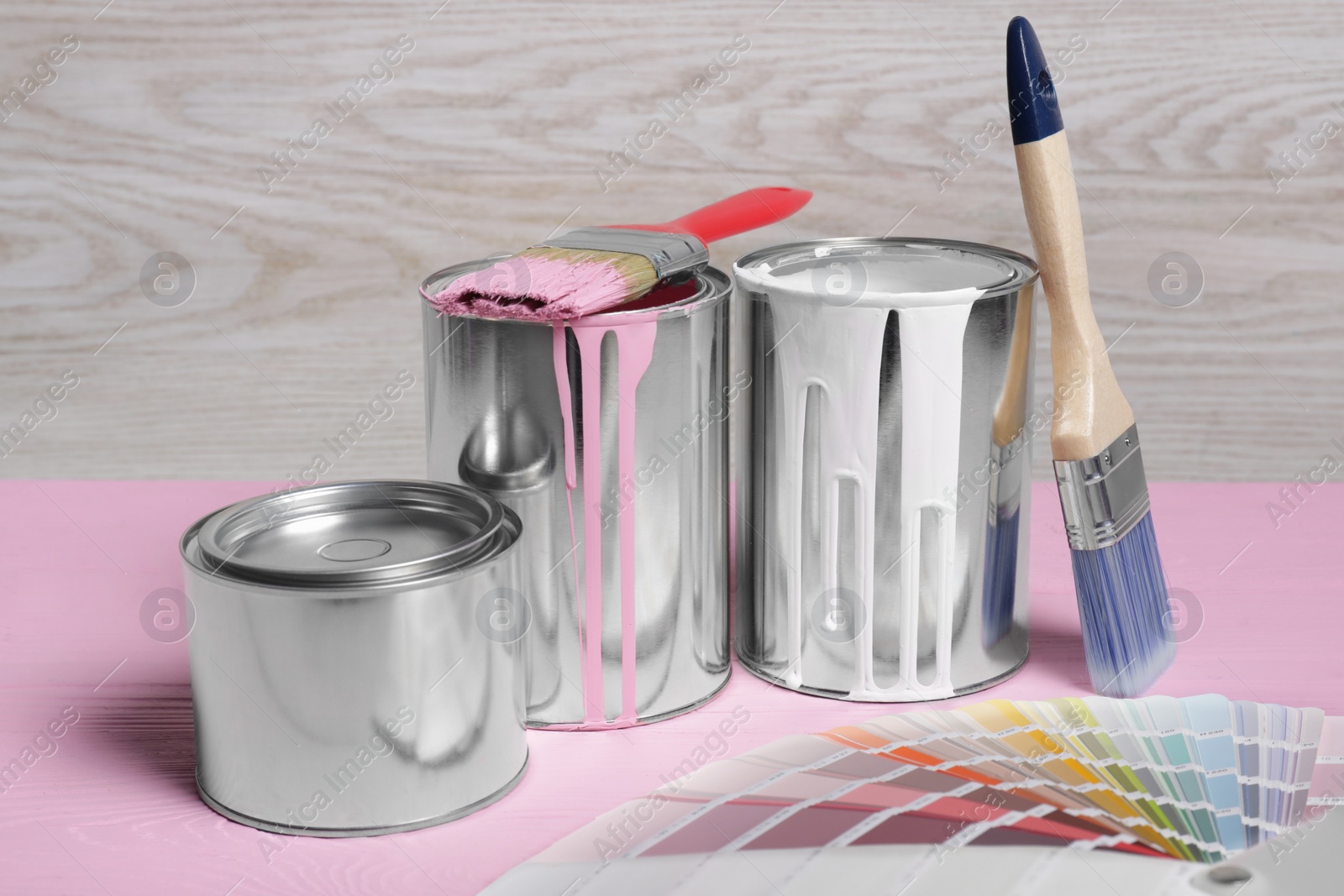 Photo of Cans of paints, brushes and color palette on pink wooden table