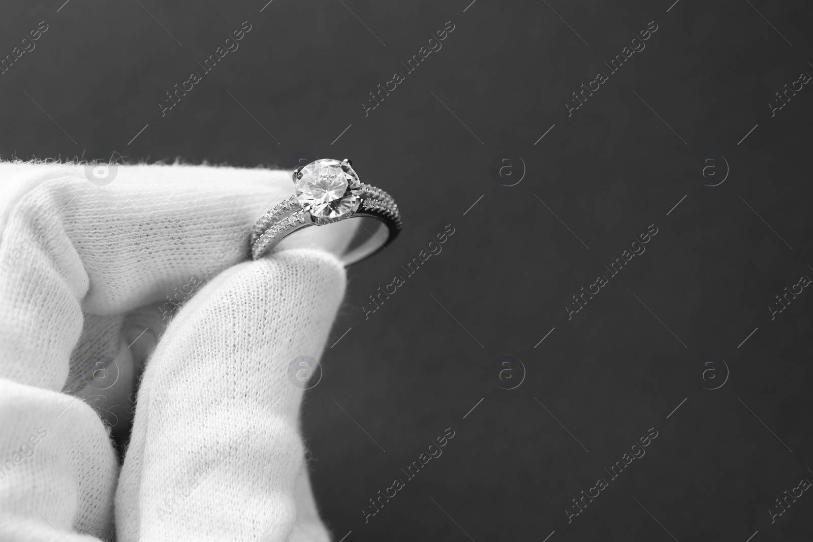 Photo of Jeweler holding diamond ring on dark grey background, closeup. Space for text