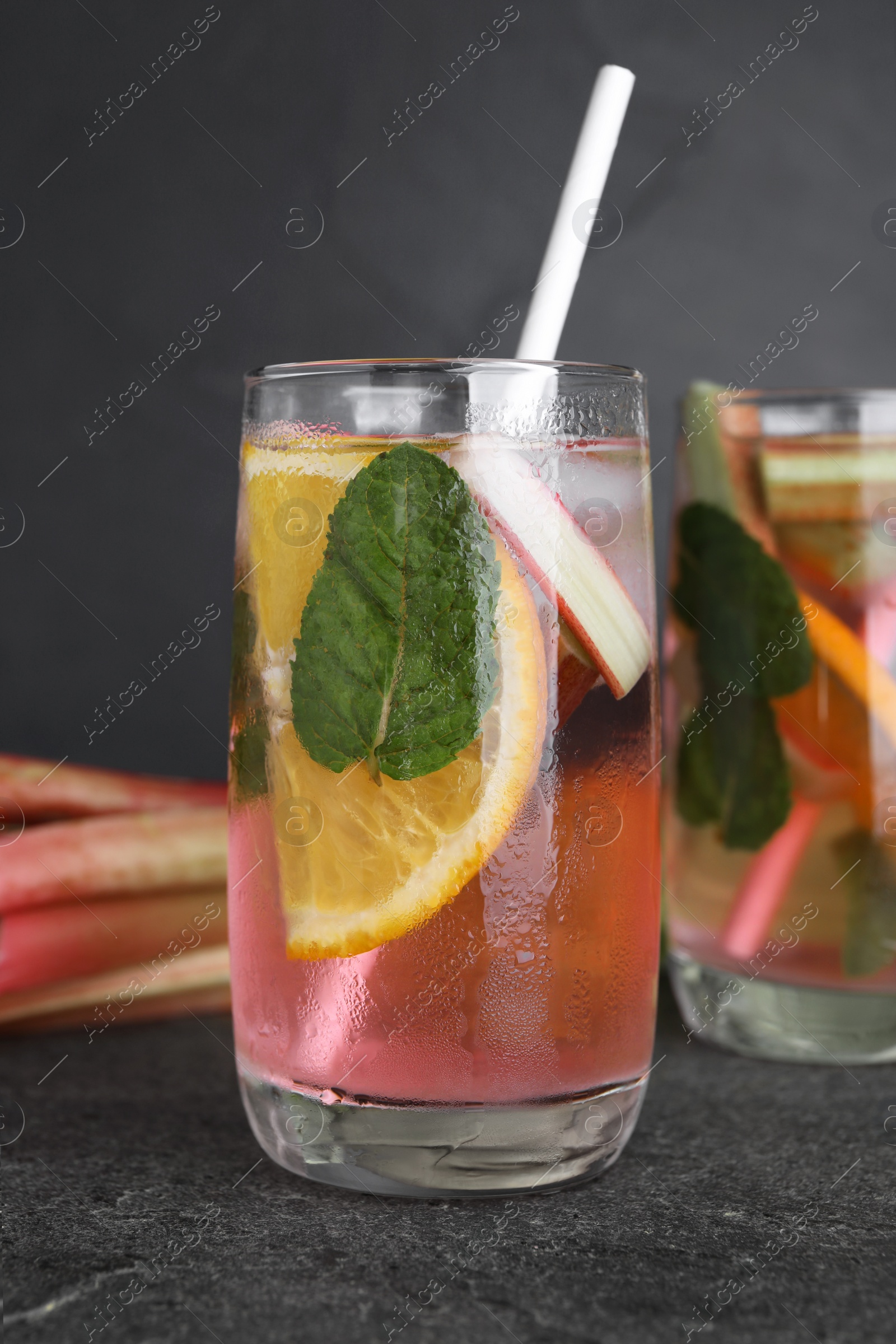 Photo of Glass of tasty rhubarb cocktail with lemon on grey table