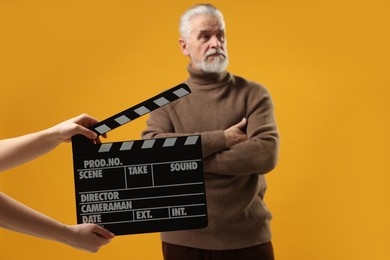 Photo of Senior actor performing while second assistant camera holding clapperboard on yellow background, selective focus. Film industry