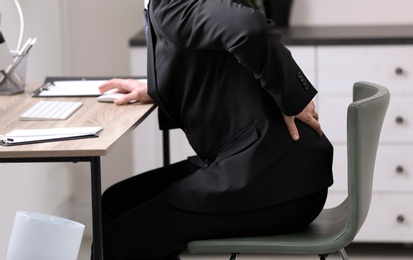 Photo of Businessman suffering from back pain at workplace, closeup