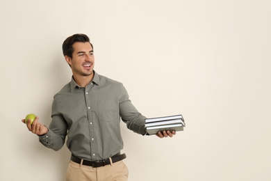 Photo of Young male teacher with books and apple on beige background. Space for text