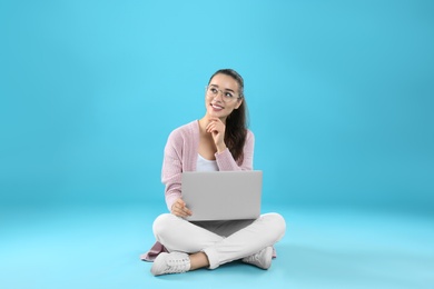 Young woman in casual outfit with laptop sitting on color background