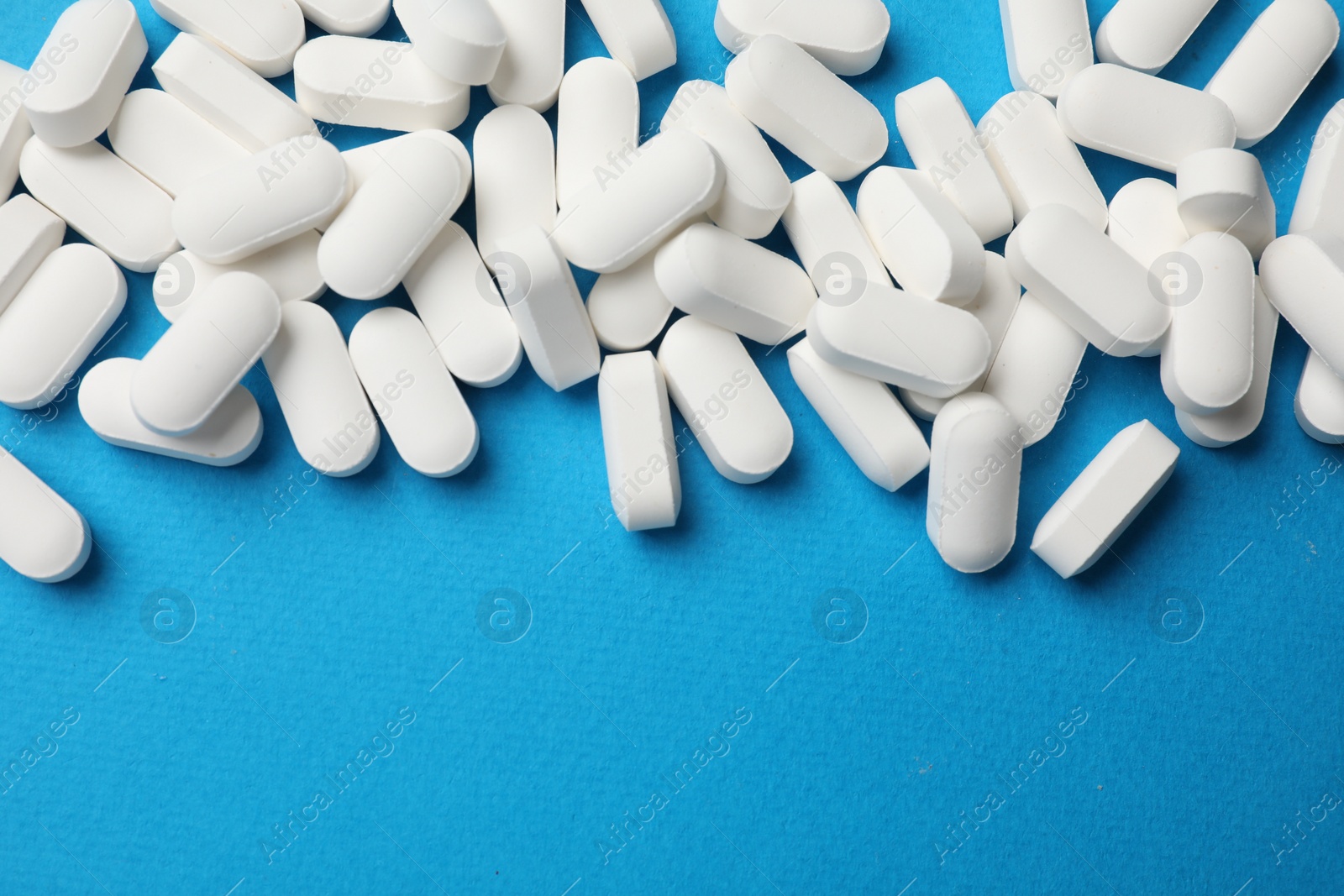 Photo of Vitamin pills on light blue background, top view. Space for text