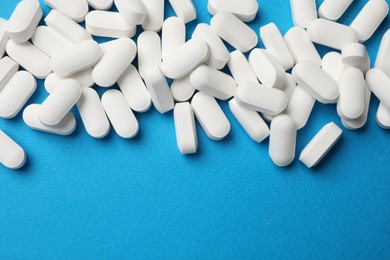 Photo of Vitamin pills on light blue background, top view. Space for text