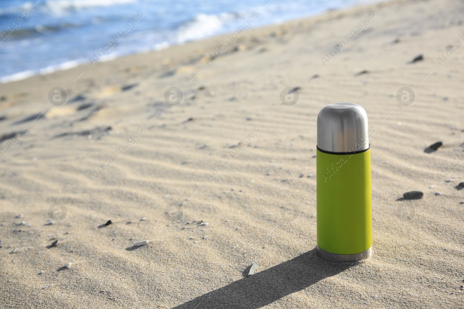 Photo of Yellow thermos with hot drink on sand near sea, space for text