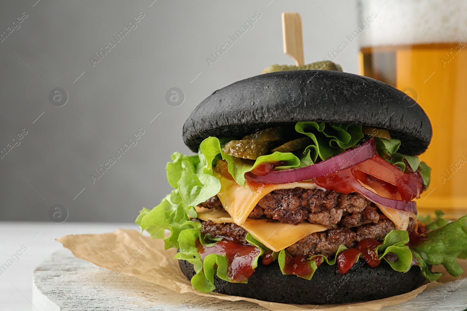 Photo of Board with black burger and beer on table. Space for text