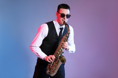 Young man in elegant outfit playing saxophone on color background