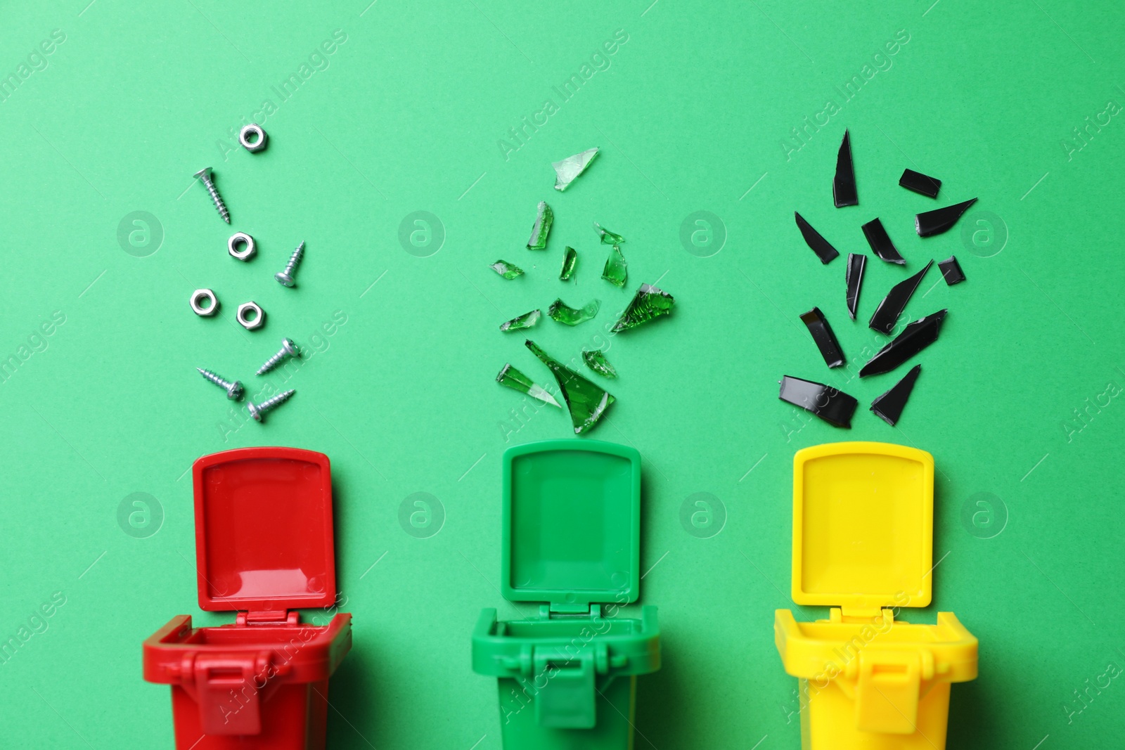 Photo of Mini recycling bins and different garbage on green background, flat lay. Waste sorting