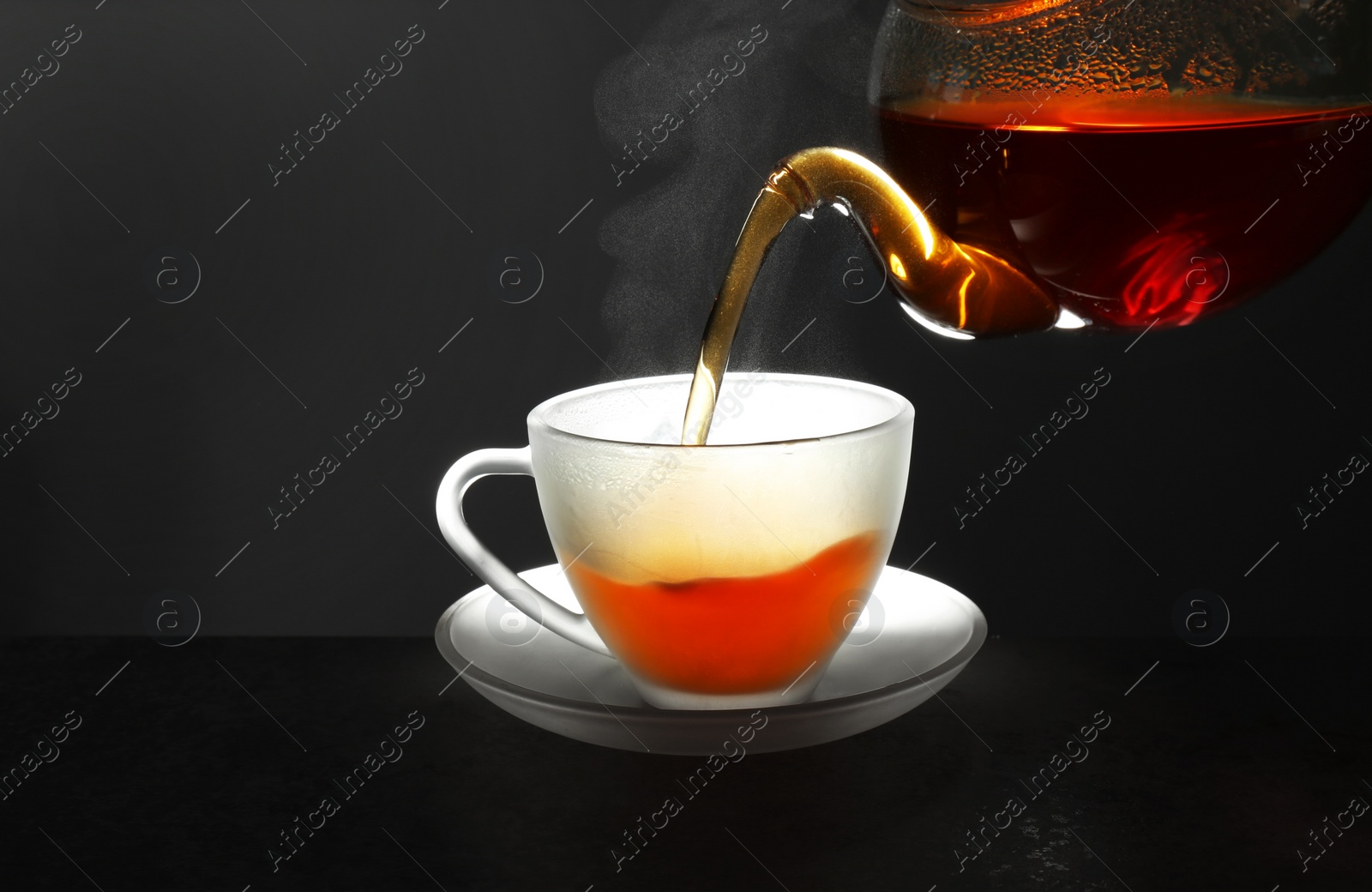 Photo of Pouring fresh hot tea into glass cup on table against grey background