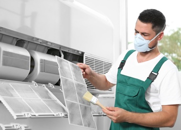 Photo of Professional male technician cleaning air conditioner indoors. Repair and maintenance