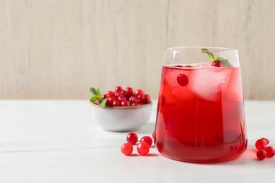 Tasty cranberry juice with ice cubes in glass and fresh berries on white wooden table, closeup. Space for text