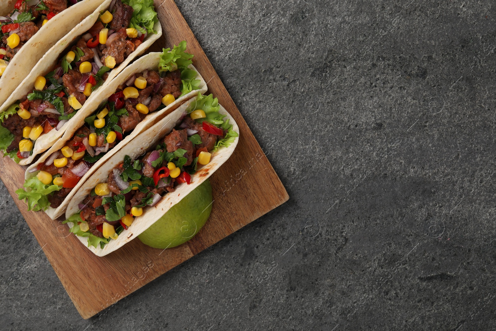 Photo of Delicious tacos with meat and vegetables on gray textured table, top view. Space for text