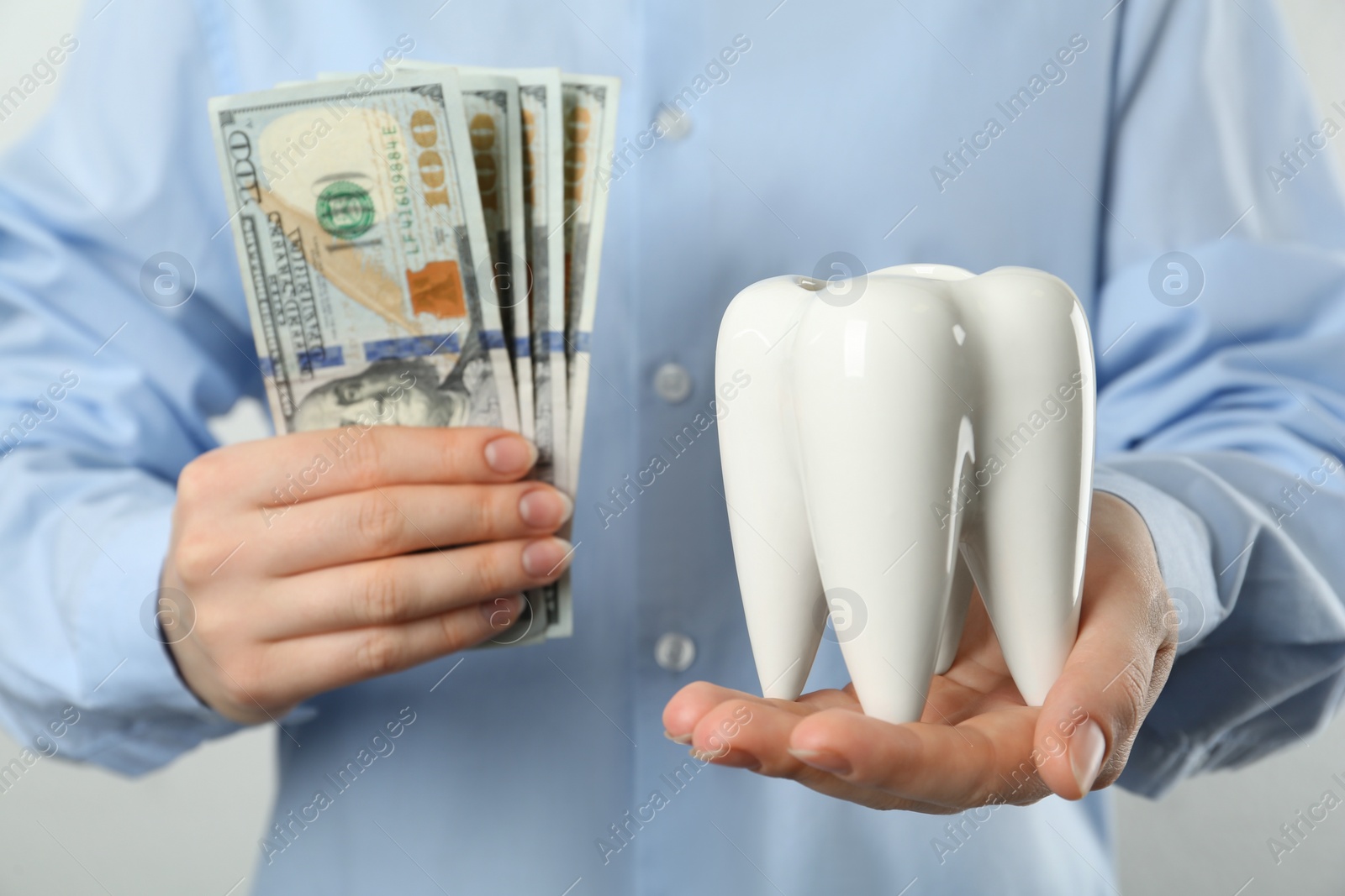 Photo of Woman holding ceramic model of tooth and dollar banknotes on light background, closeup. Expensive treatment