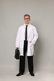 Photo of Doctor in glasses holding briefcase on grey background