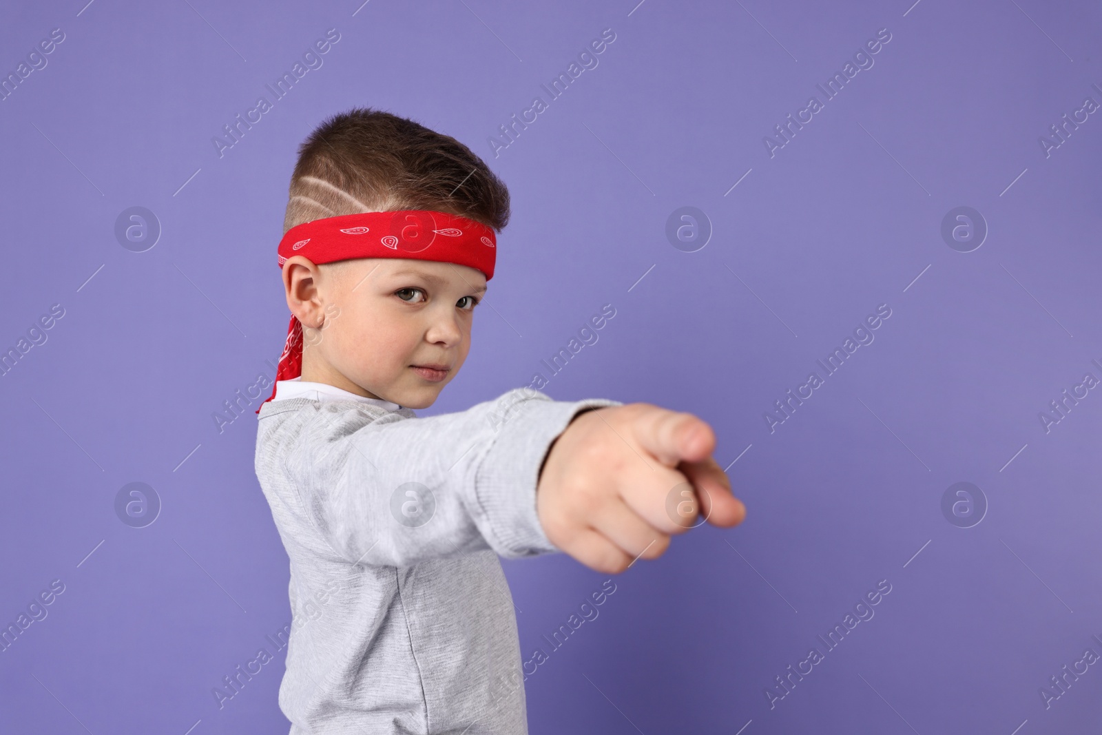 Photo of Happy little boy pointing at something on violet background. Space for text