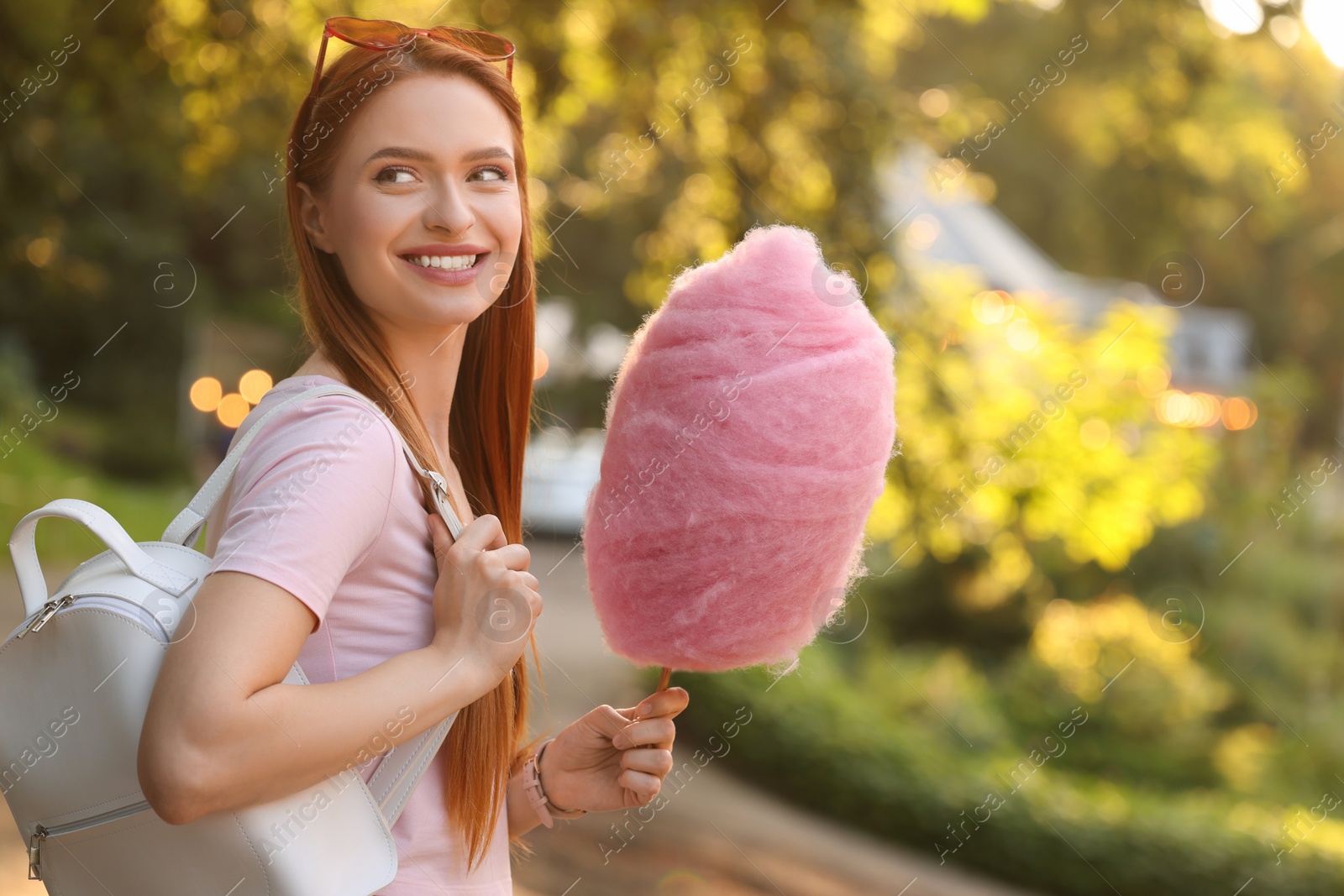 Photo of Smiling woman with cotton candy outdoors on sunny day. Space for text